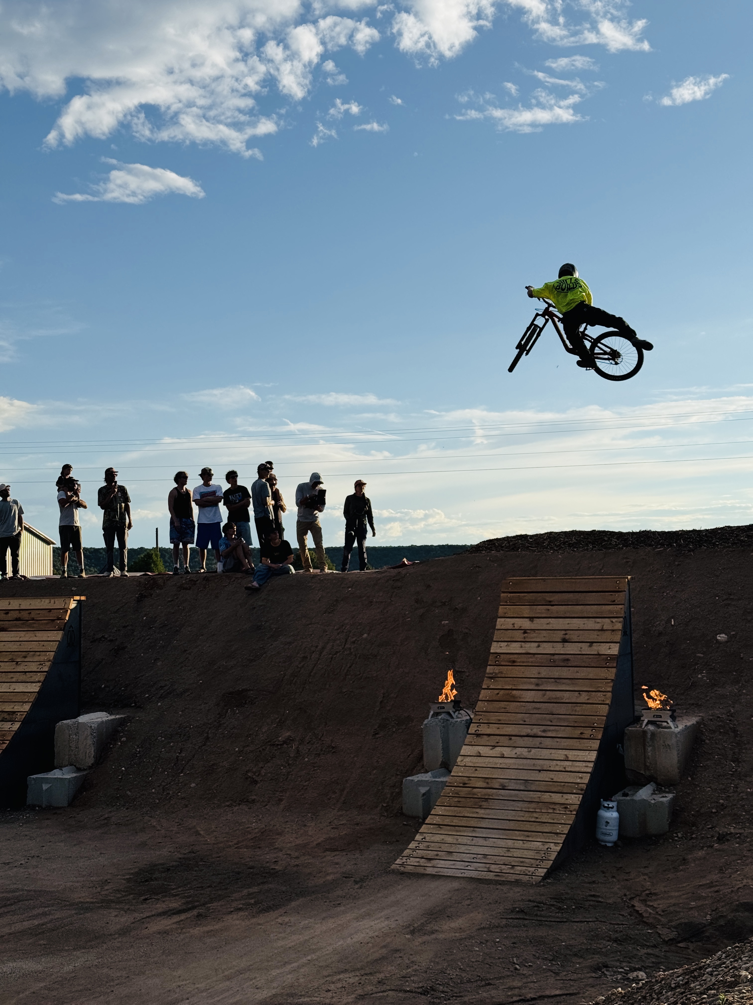 Rider sending a whip over the jump at Picuris Pueblo All-Wheel Park — fire pits and crowd